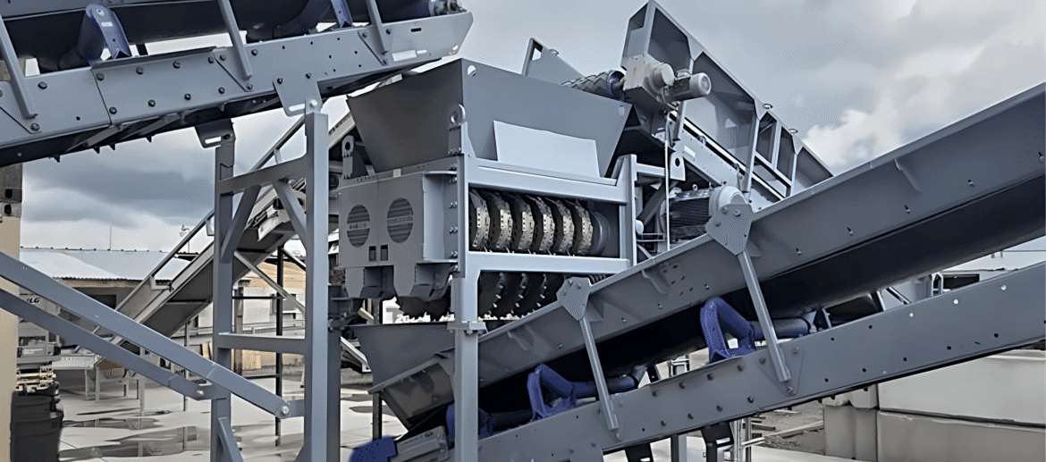 dual-shaft-shredder dual-shaft twin tire shredder with circular cutting barclay knives, fed by an inclined conveyor at an outdoor recycling site.